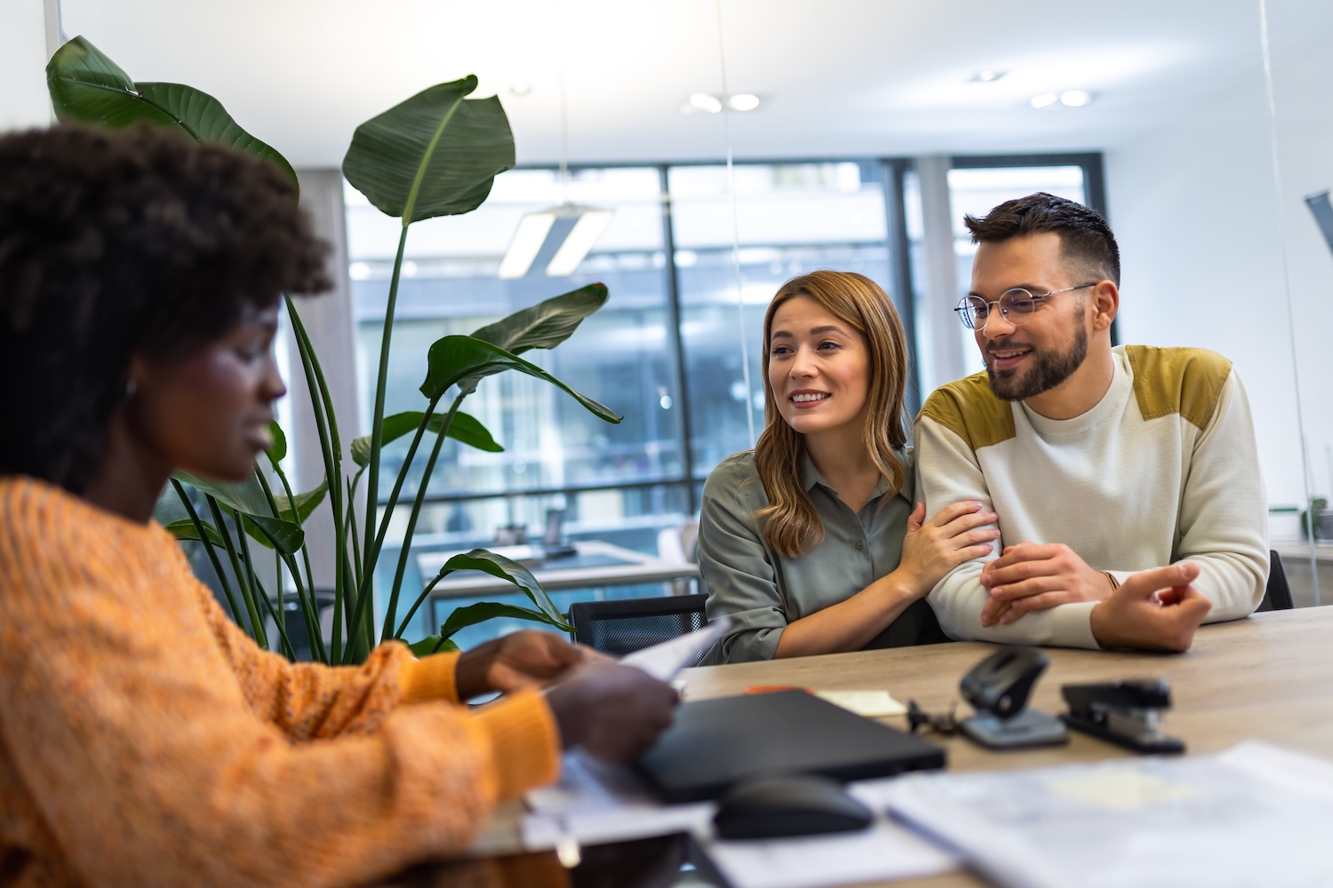Un couple est assis à un bureau, face à une professionnelle qui fournit des informations ou des documents.