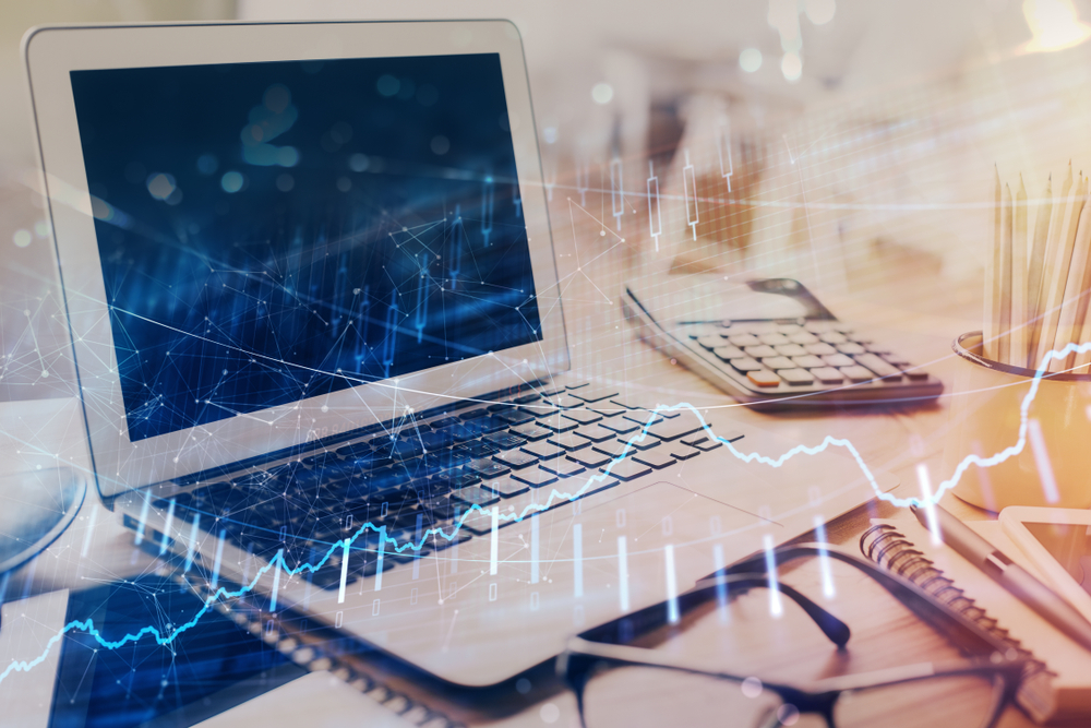 Un ordinateur portable, une calculatrice, un bloc-notes et des lunettes sur un bureau avec des graphiques financiers abstraits superposés.