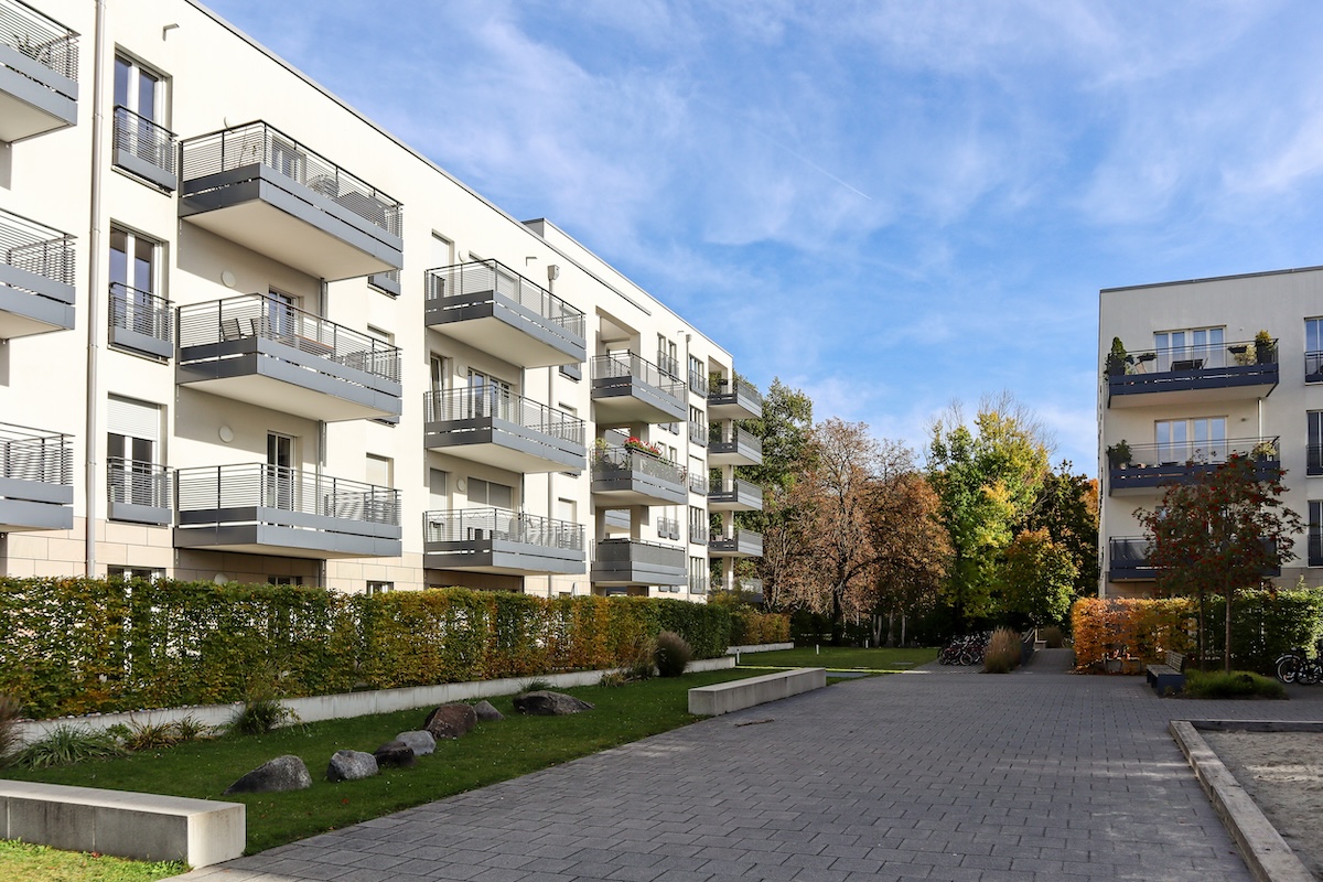 Immeubles d'appartements modernes avec balcons et allée pavée. La pelouse et les buissons sont au premier plan, tandis que les arbres au feuillage d'automne sont à l'arrière-plan.
