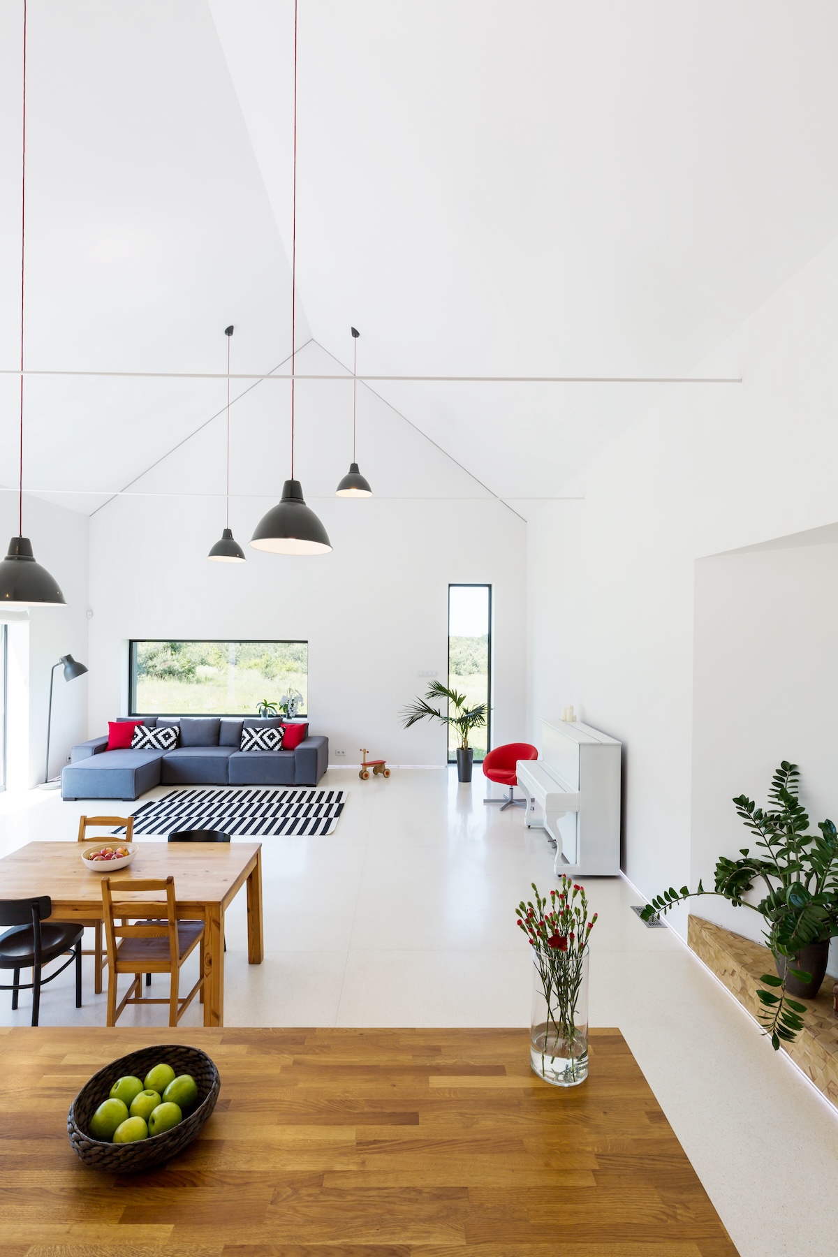 Un espace de vie moderne à aire ouverte avec des murs blancs, des meubles en bois, des luminaires suspendus, un tapis noir et blanc et une décoration minimaliste. Un bol de pommes vertes est posé sur la table à manger en bois.